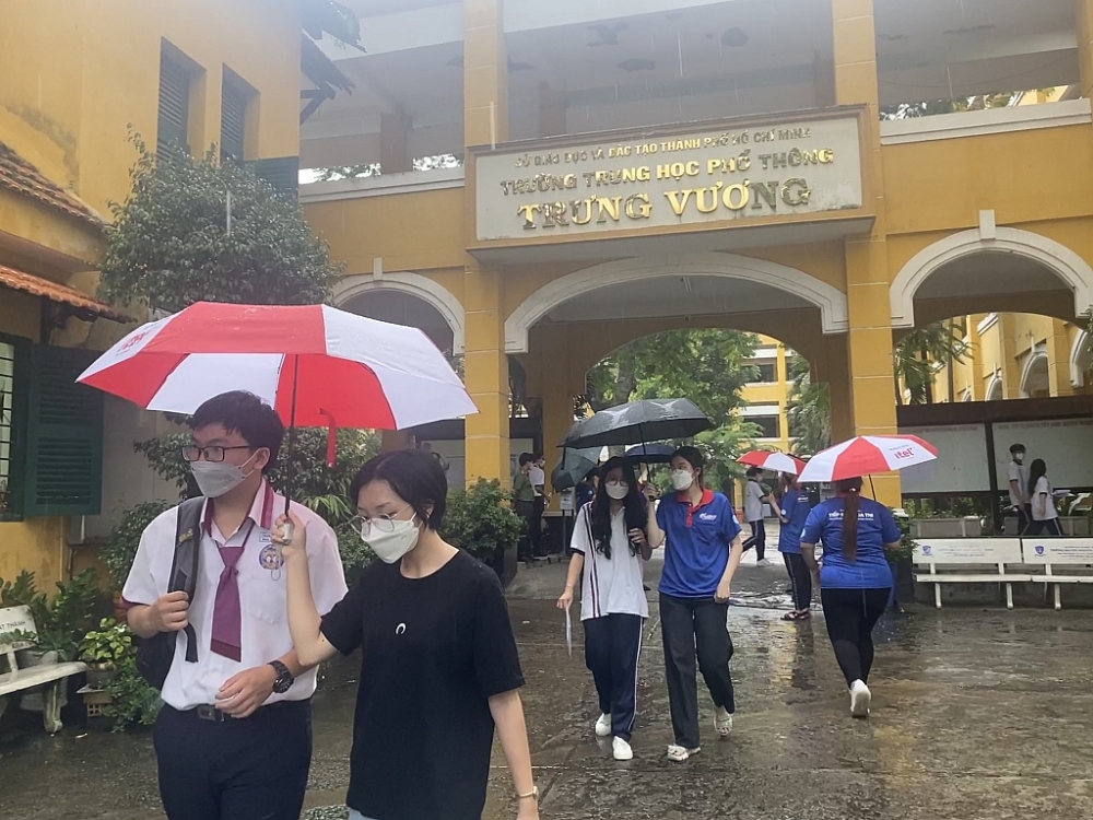Các tình nguyện viên che mưa cho thí sinh ra về tại điểm thi Trường THPT Trưng Vương (quận 1, TPHCM).